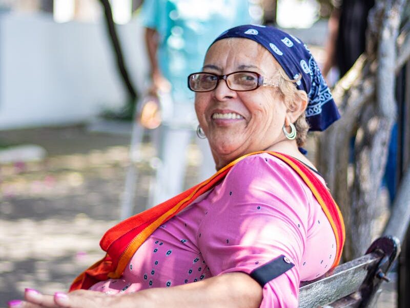Cheerful senior woman with eyeglasses sitting on a park bench outdoors.