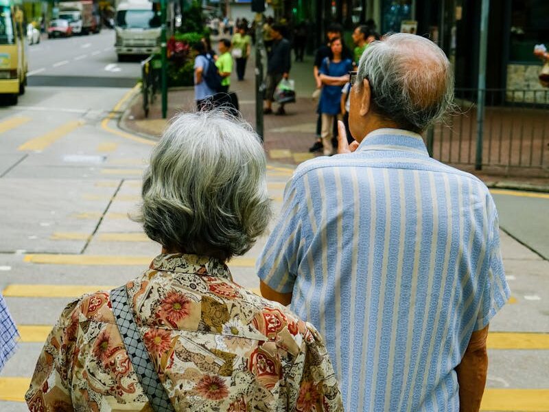 Senior couple waiting at a crosswalk in urban Kowloon, Hong Kong, during the day.