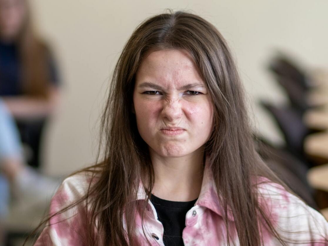 An angry teenage girl sitting in a classroom, displaying a frustrated expression.