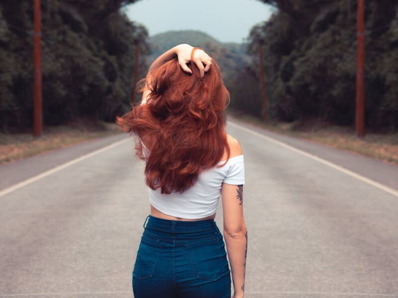 Red-haired woman in jean shorts walking down a forest road, showcasing style and freedom.