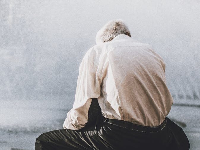 Senior man in meditation sitting on a boulder by a fountain, reflecting peacefully outdoors.
