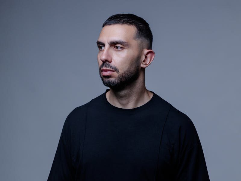 Studio portrait of a thoughtful man in a black t-shirt with a neutral background.