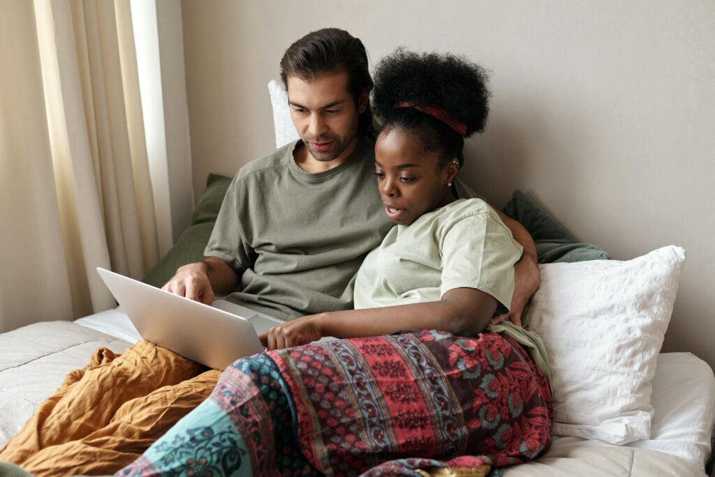 A couple enjoying leisure time together on a bed using a laptop, signifying modern relaxation.