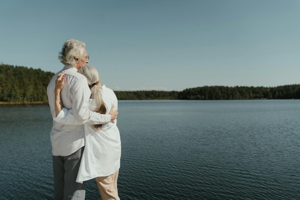 A senior couple sharing a loving embrace by a serene lakeside, symbolizing enduring love.