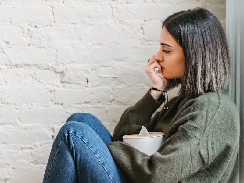 Young woman sitting in a pensive mood with tissues, expressing contemplation and emotion.