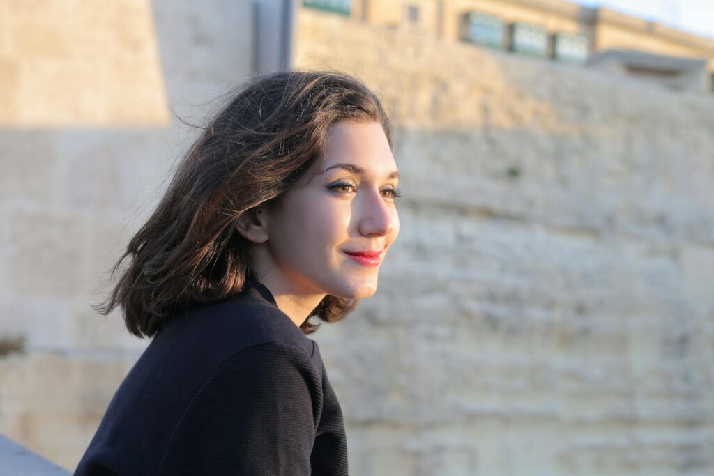 A young woman smiling outdoors near a historical stone wall in Mgarr, Malta.