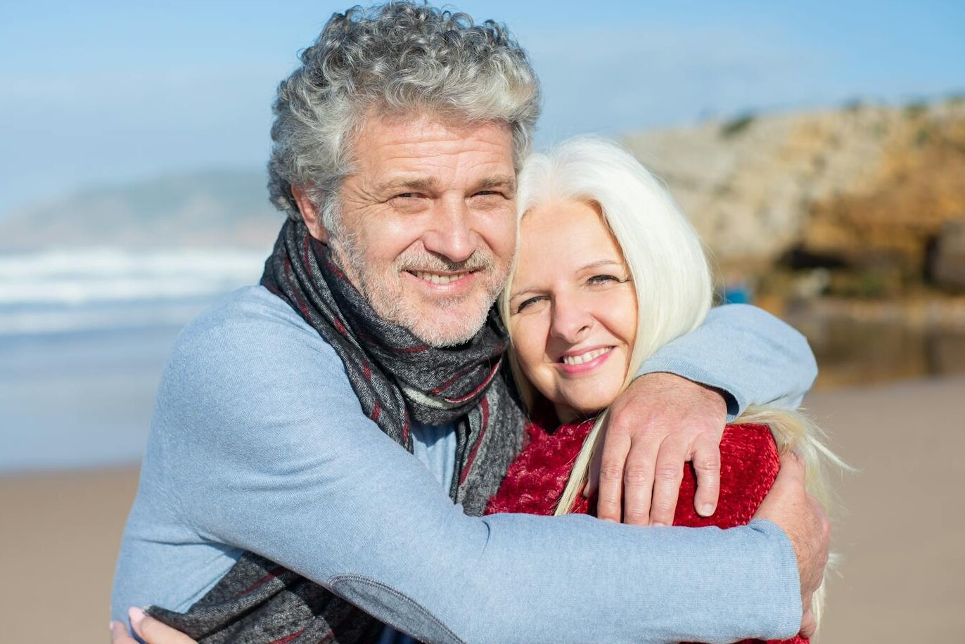 Joyful elderly couple hugging on a sunny beach in Portugal, enjoying a romantic day.