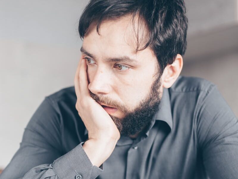 A worried man in a gray shirt holds a credit card, symbolizing online fraud or financial stress.