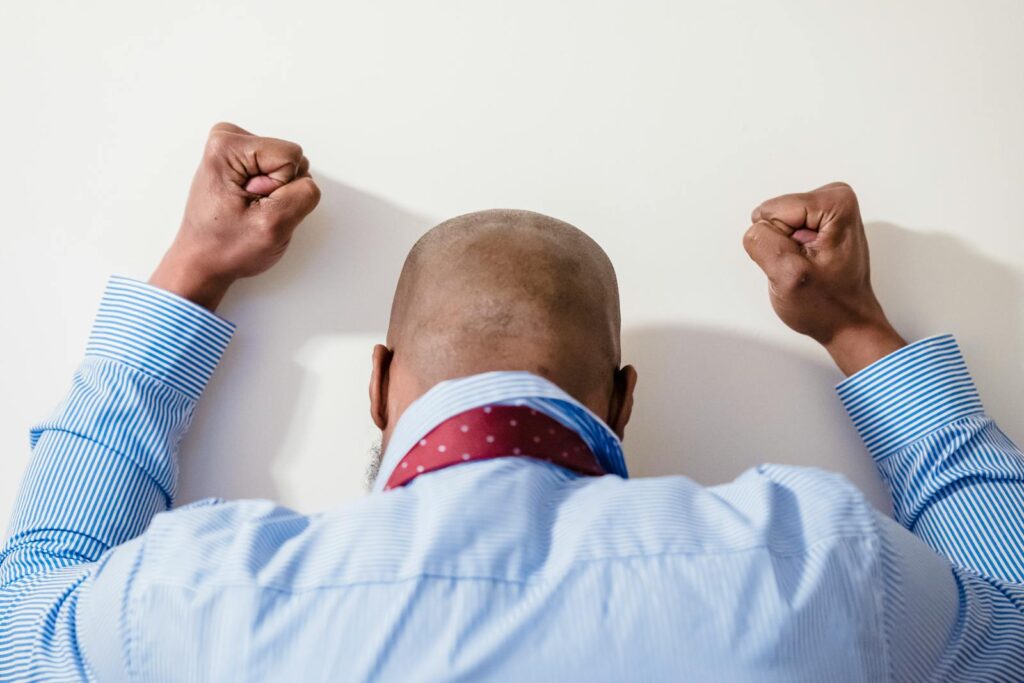 A bald man in a blue striped shirt with clenched fists expressing frustration against a white background.