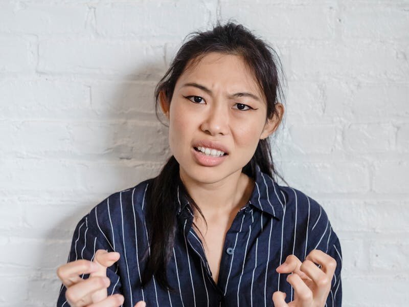 Portrait of a woman expressing frustration against a white brick wall, conveying strong emotions.