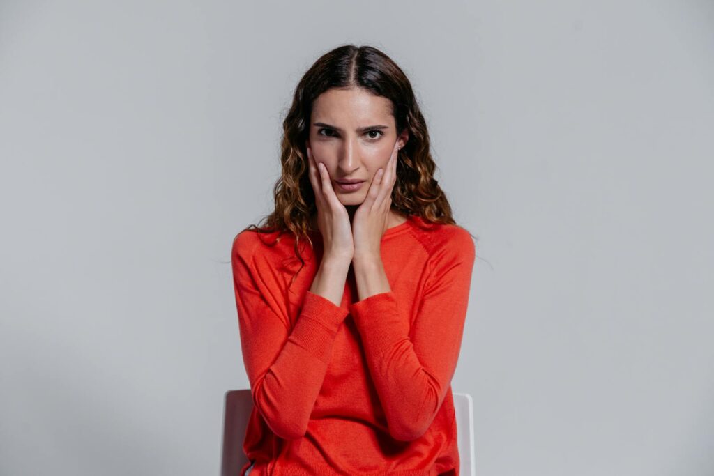 Adult woman sitting indoors with a contemplative facial expression, wearing a red sweater.