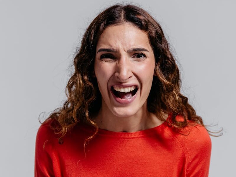 Portrait of a young woman in a red sweater expressing emotion indoors.