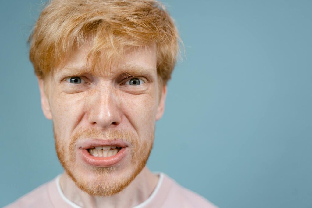 Close-up of a redhead man showing an intense facial expression against a blue background.
