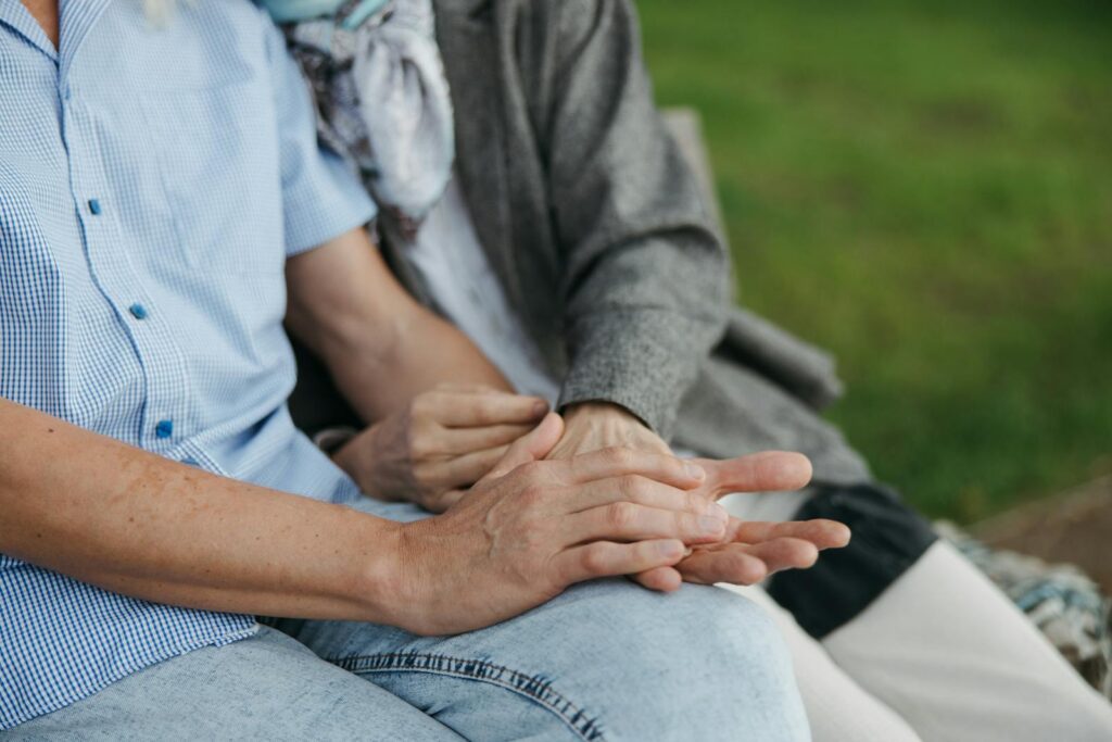 Close-up of elderly couple holding hands on a bench, symbolizing love and companionship.