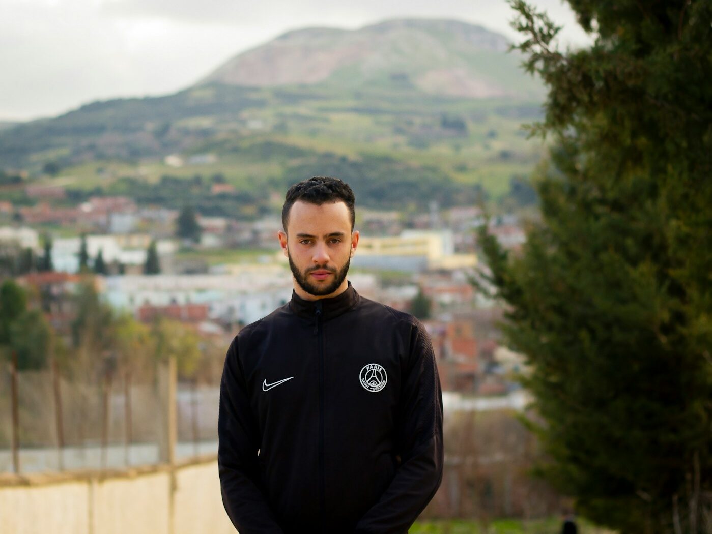 man in black hoodie standing near green trees during daytime