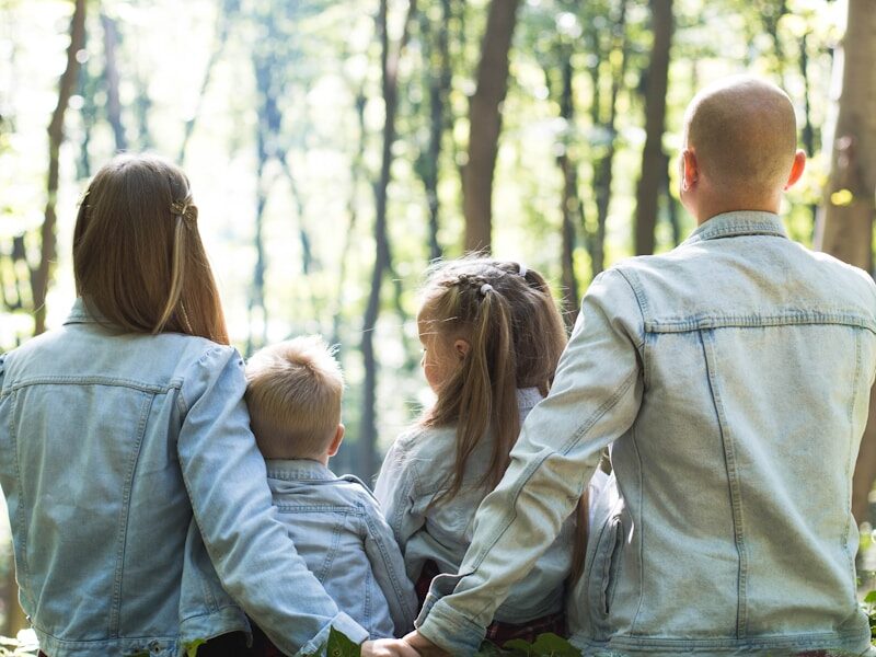 man and woman holding hands together with boy and girl looking at green trees during day