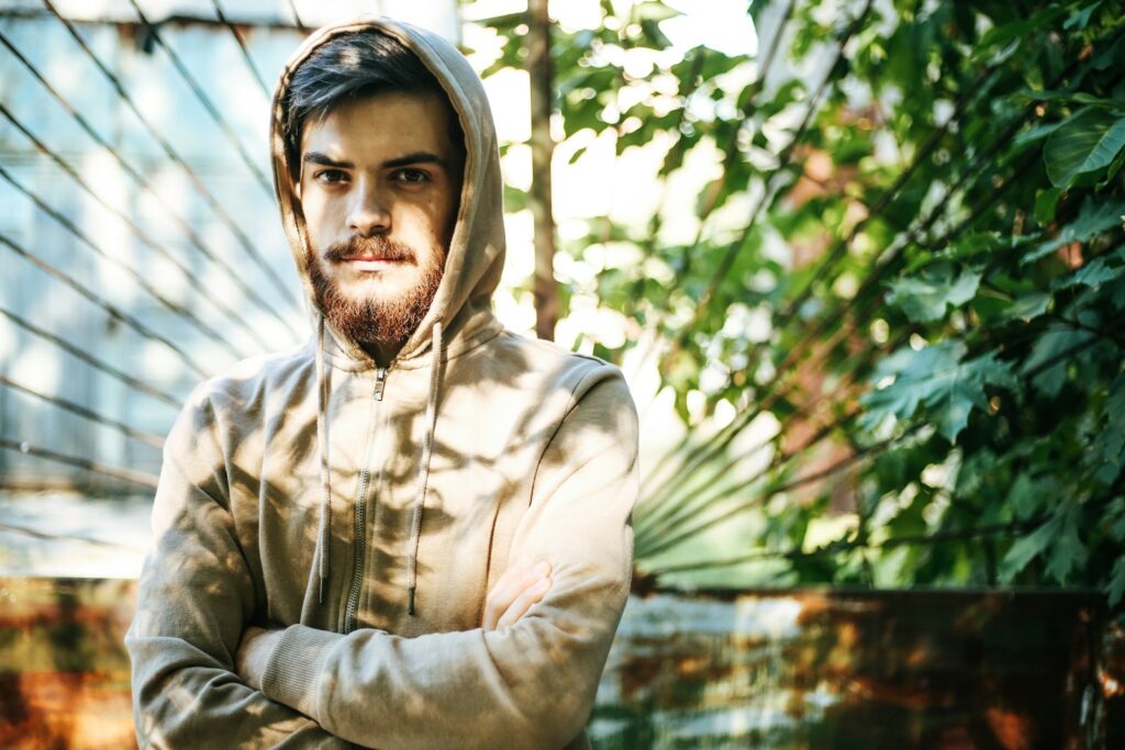man in brown zip up hoodie standing near green leaf tree during daytime