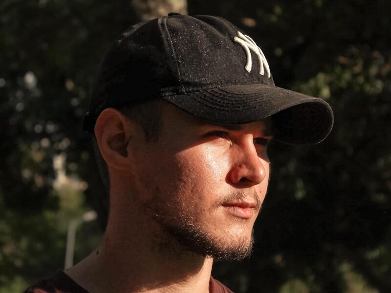 a man wearing a hat standing in front of a tree