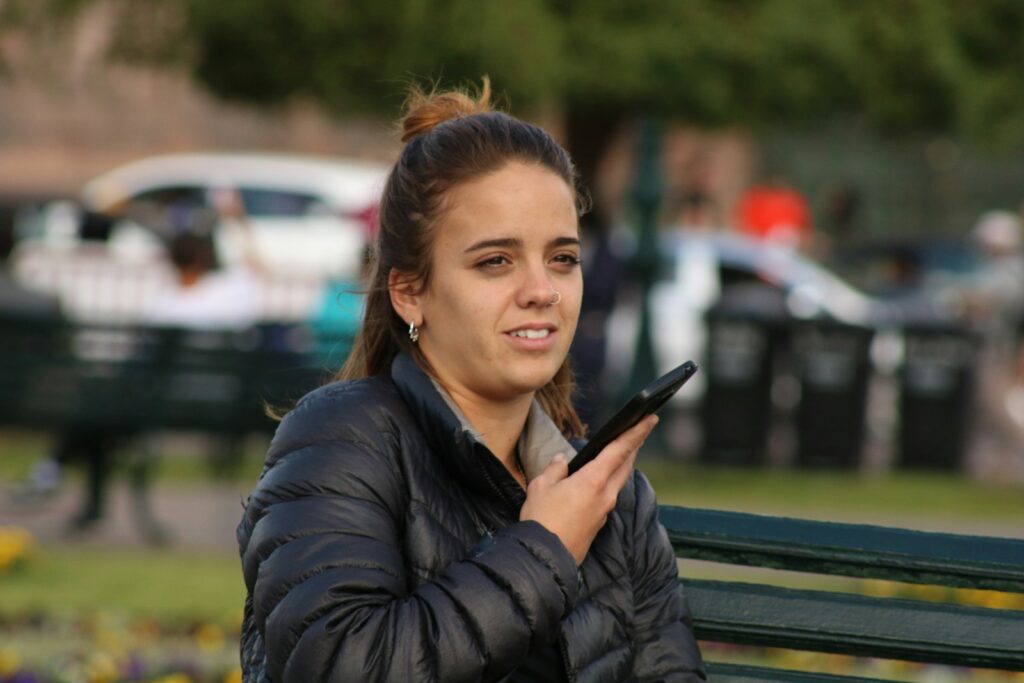man in black bubble jacket holding smartphone while sits on bench