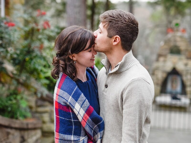 man kissing on woman forehead standing near tree during daytime