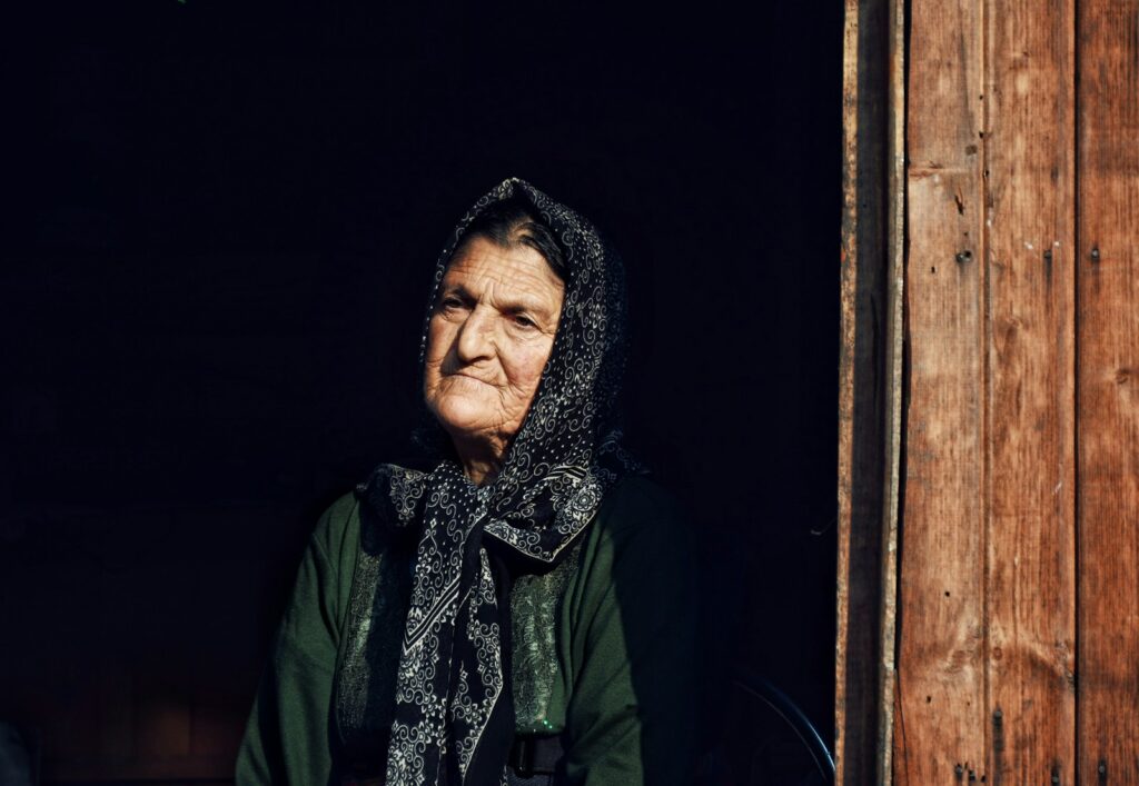 an old woman with a scarf on her head looking out a window