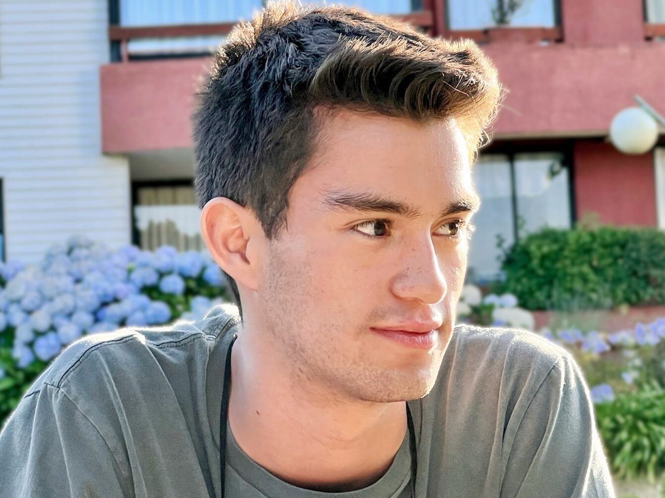 a man with a short haircut sitting in front of a building