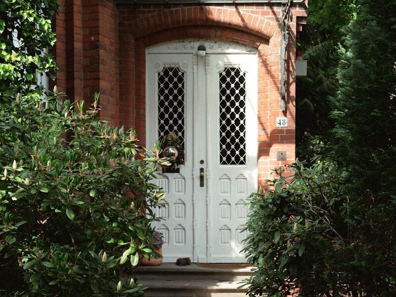 a brick house with a white door surrounded by greenery