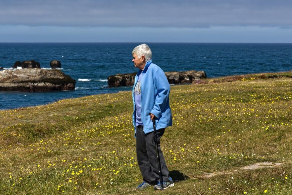 man in blue jacket standing on green grass field near body of water during daytime