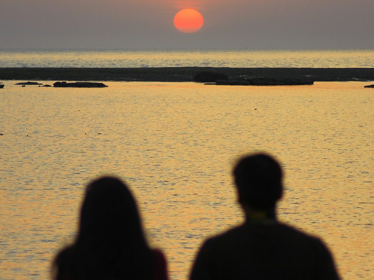 silhouette of 2 person standing on seashore during sunset