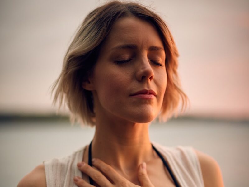woman in white vest and black bikini with hand on chest