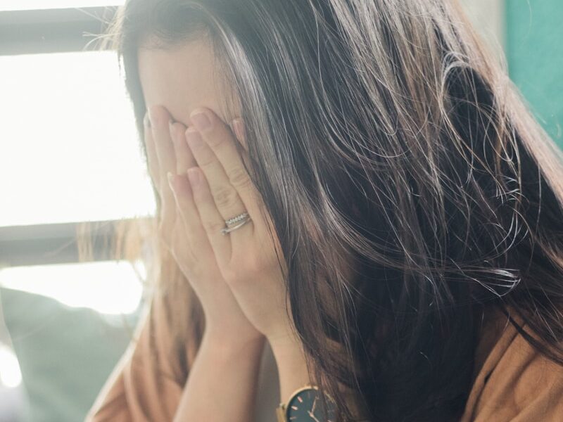 woman in brown shirt covering her face