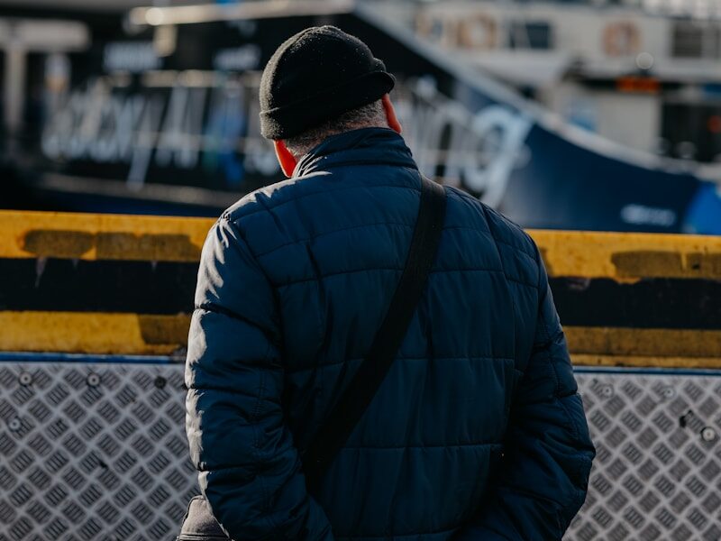 A man standing next to a fence with a boat in the background