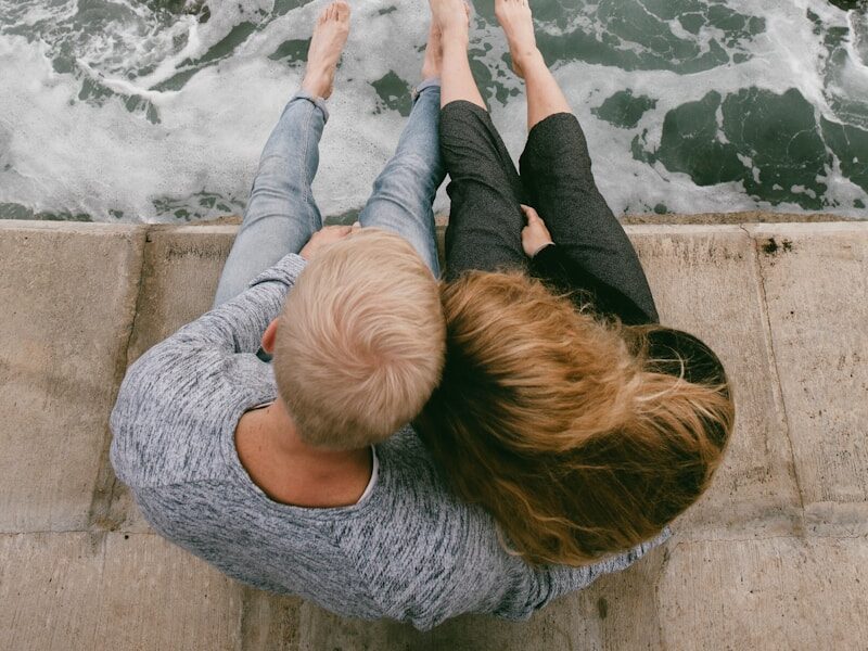 man and woman sitting on cliff near body of water