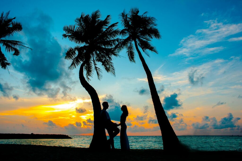 Silhouette of a couple between palm trees on a tropical beach at sunset, depicting romance and tranquility.