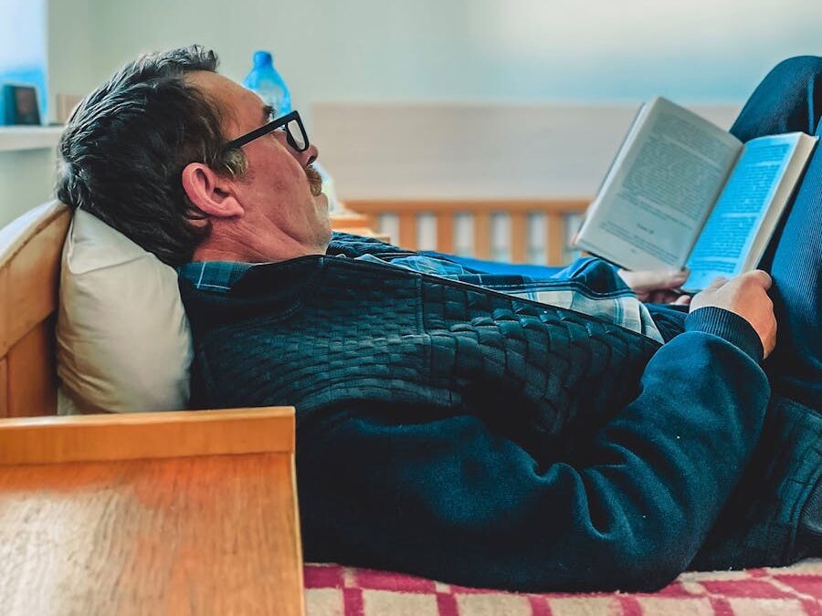 Elderly man reading a book while relaxing on a comfortable bed indoors.