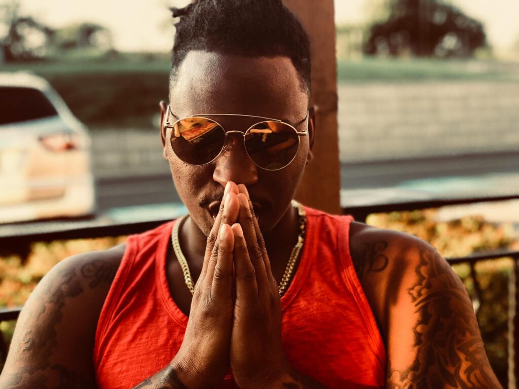 Profile of a man in sunglasses praying outdoors with a serene background.