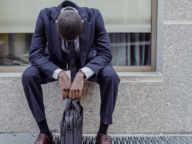 A businessman in a suit sits with his head down, expressing sadness and stress.