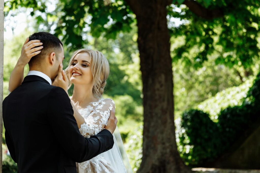 Bride and groom sharing a tender moment under a tree in a Parisian garden.