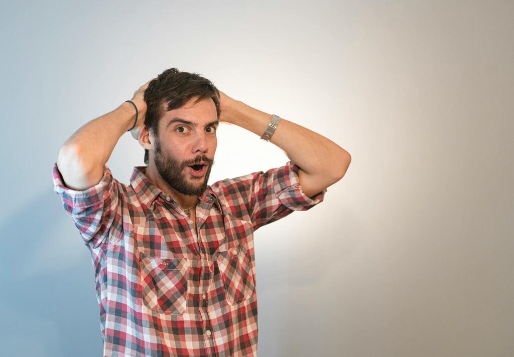 A surprised man with a beard, holding his head in astonishment in a studio setting.