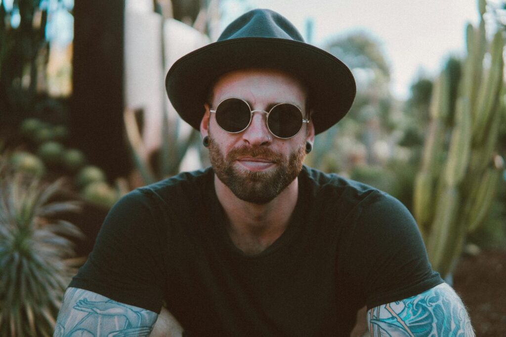 Stylish man with beard and tattoos wearing sunglasses and a hat, enjoying outdoors.