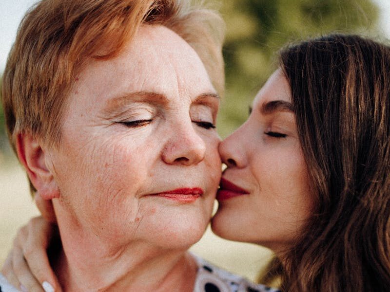 A tender moment of a woman kissing her mother on the cheek outdoors, symbolizing love and connection.
