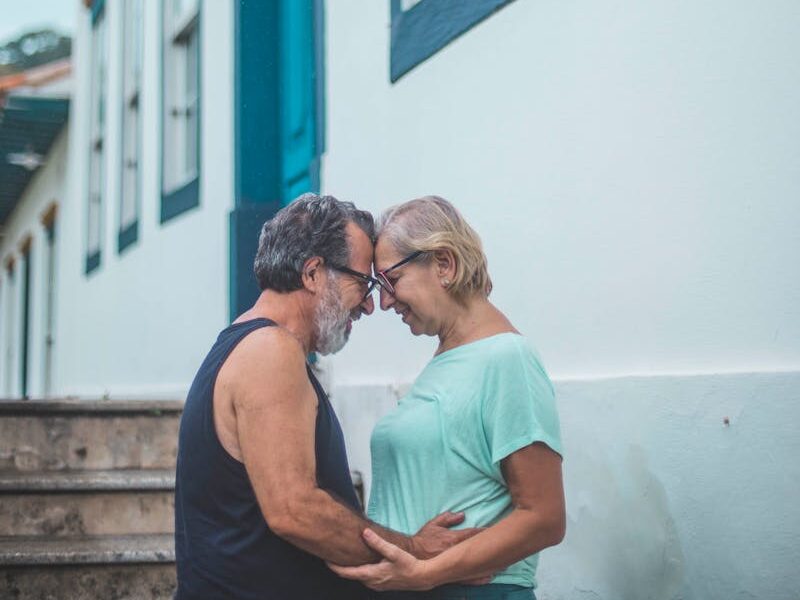Senior couple sharing a tender moment outdoors by a blue and white house.