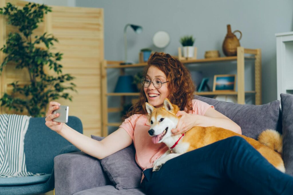 Cheerful woman taking a selfie with her Shiba Inu dog on a comfortable sofa at home.