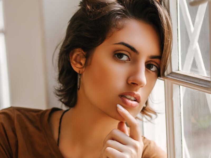 Graceful portrait of a thoughtful woman leaning against a window, capturing natural beauty and introspection.