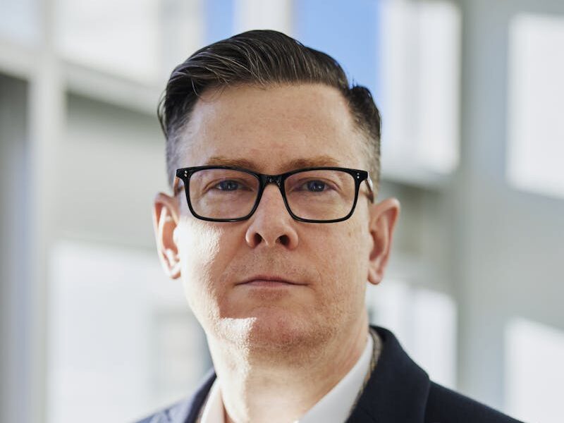 Profile portrait of a confident business executive wearing eyeglasses in a sunlit office setting.
