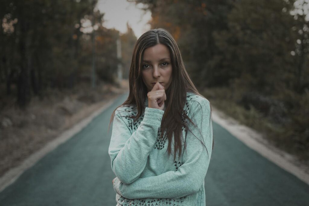 Pensive woman standing on a quiet forest road, lost in thought. Outdoor portrait.