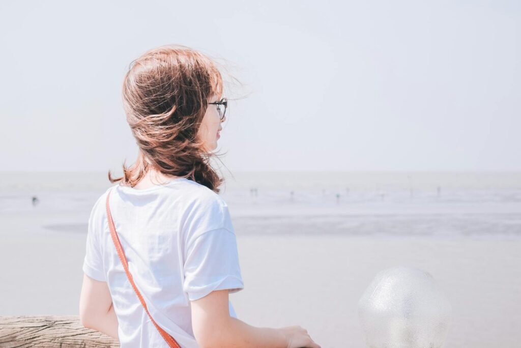 Back view of a woman standing by the seashore, reflecting on a windy day.