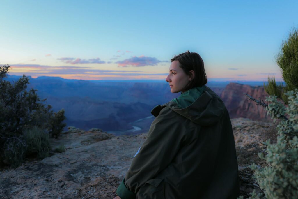 A contemplative woman sitting at the Grand Canyon rim during sunset, capturing a serene outdoor moment.