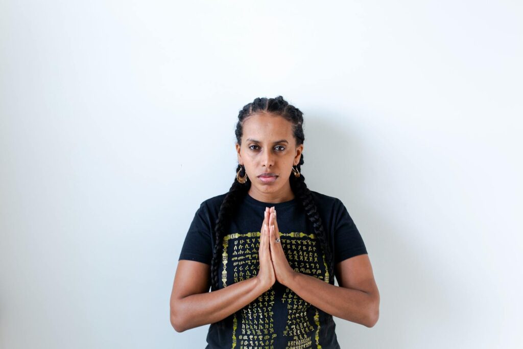 Young woman with braided hair performs a praying gesture in a calm studio setting.