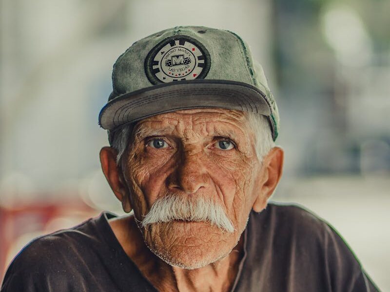 Portrait of an elderly man with a mustache, wearing a cap and serious expression, outdoors.